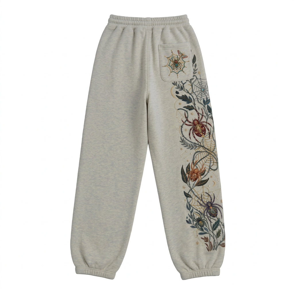 Light gray heather sweatpants with a spider-themed floral embroidery design running down the right leg and a matching spider motif on the pocket, shown against a solid black background.