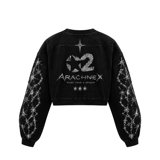Black cropped denim-style sweatshirt shown from the back, featuring a large distressed silver graphic reading 'X2 Arachnex' with smaller text 'More Than A Spider' and silver starburst line-art printed down both sleeves, on a light gray background.